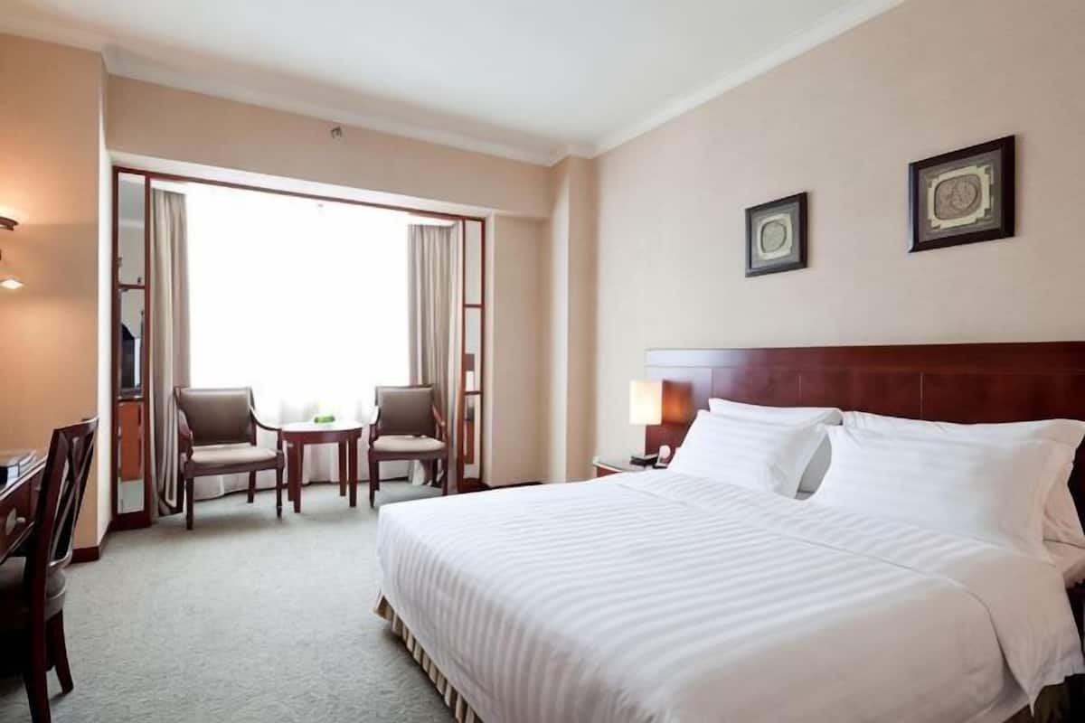 A hotel room with a large bed, a desk with a chair, a small table, and a view through a door.