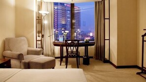 A hotel room with a bed, a desk with a chair, a lamp, and a view of a cityscape at night. - Rosedale Hotel & Suites (Guangzhou)