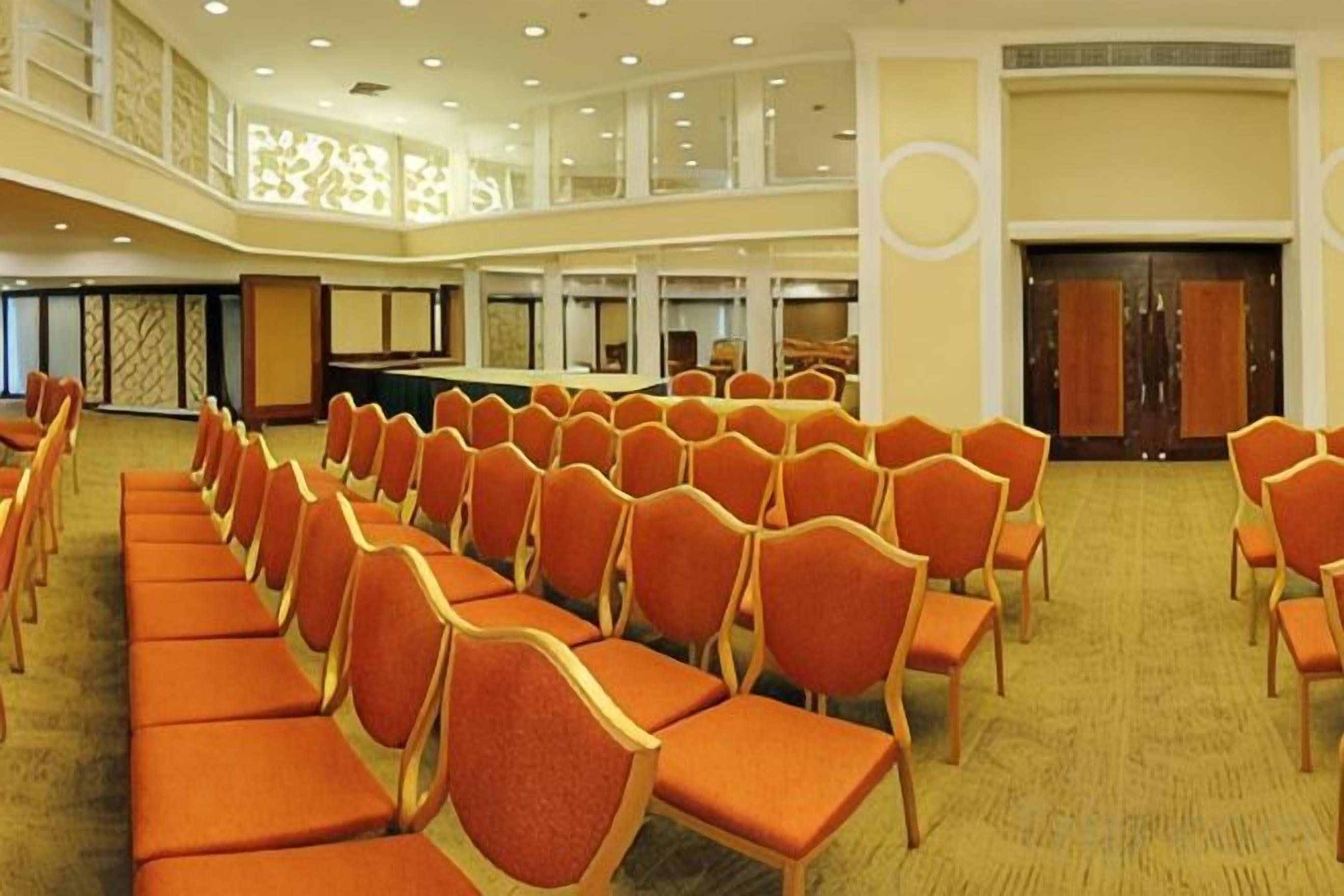Un salón de conferencias con filas de sillas, un escenario y un techo alto con iluminación empotrada.