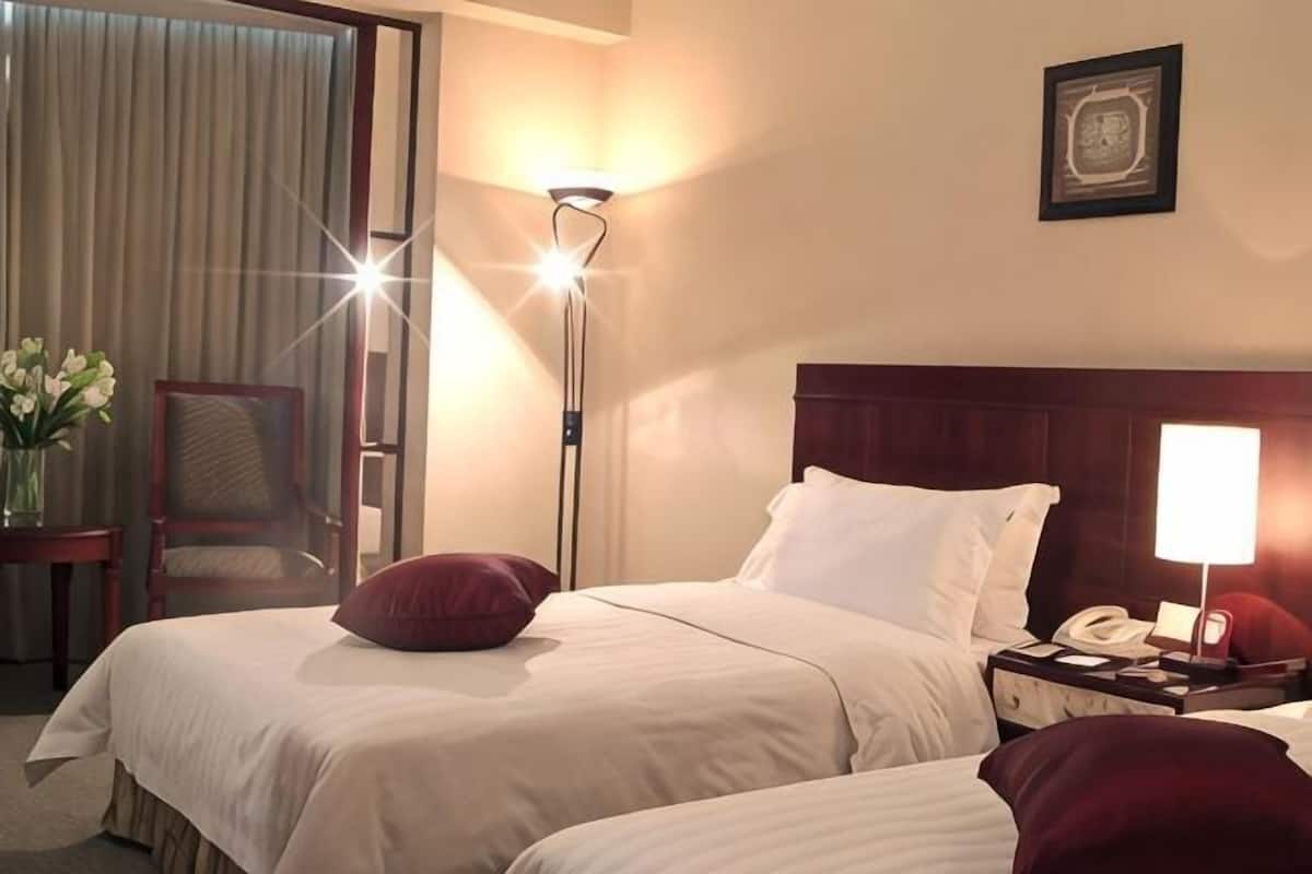 A hotel room with two beds, a nightstand with a phone, a lamp, a chair, and a curtain.