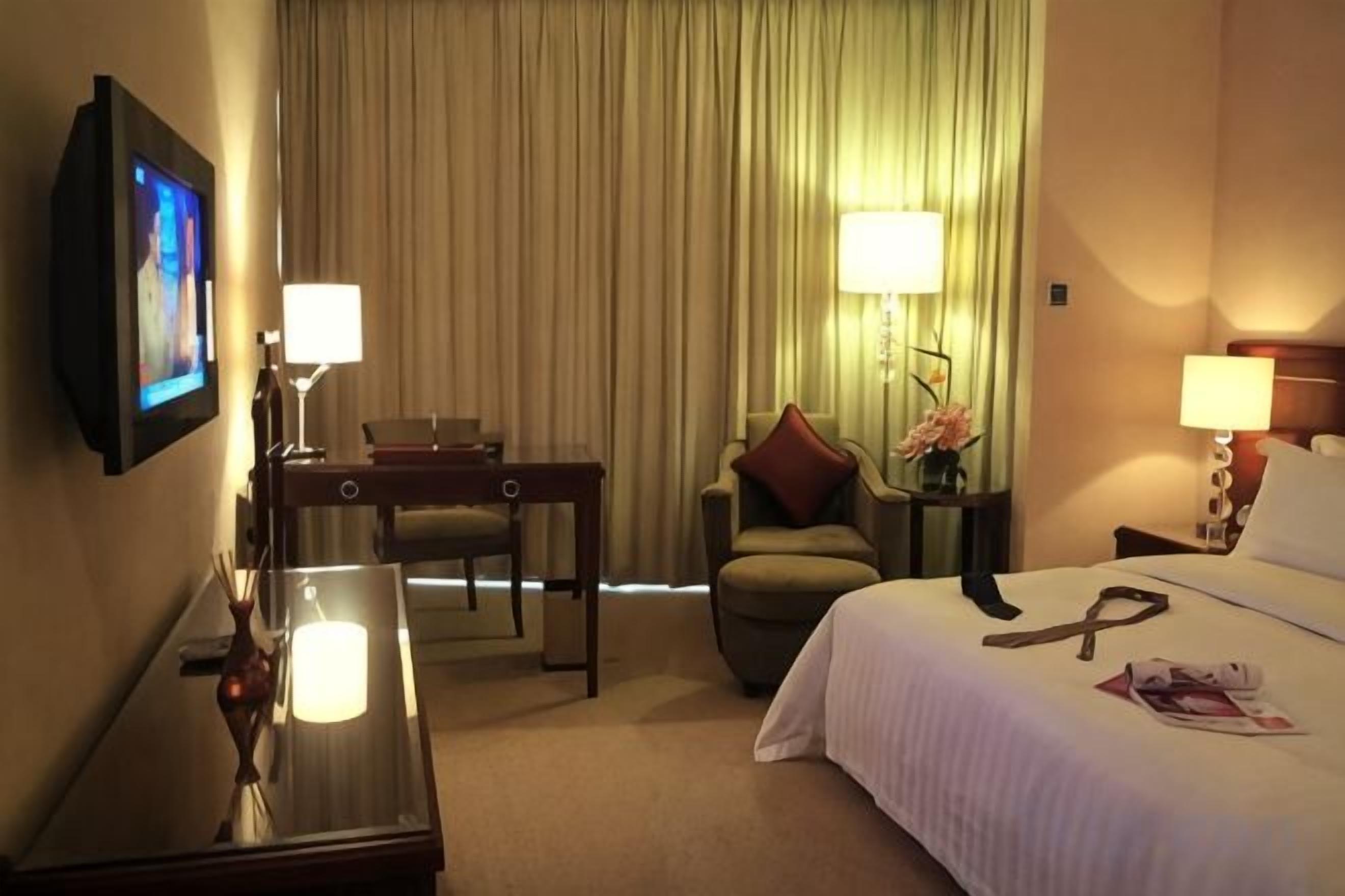 A hotel room with a bed, a desk, a chair, a television, and a window with curtains.