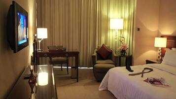 A hotel room with a bed, a desk, a chair, a television, and a window with curtains.