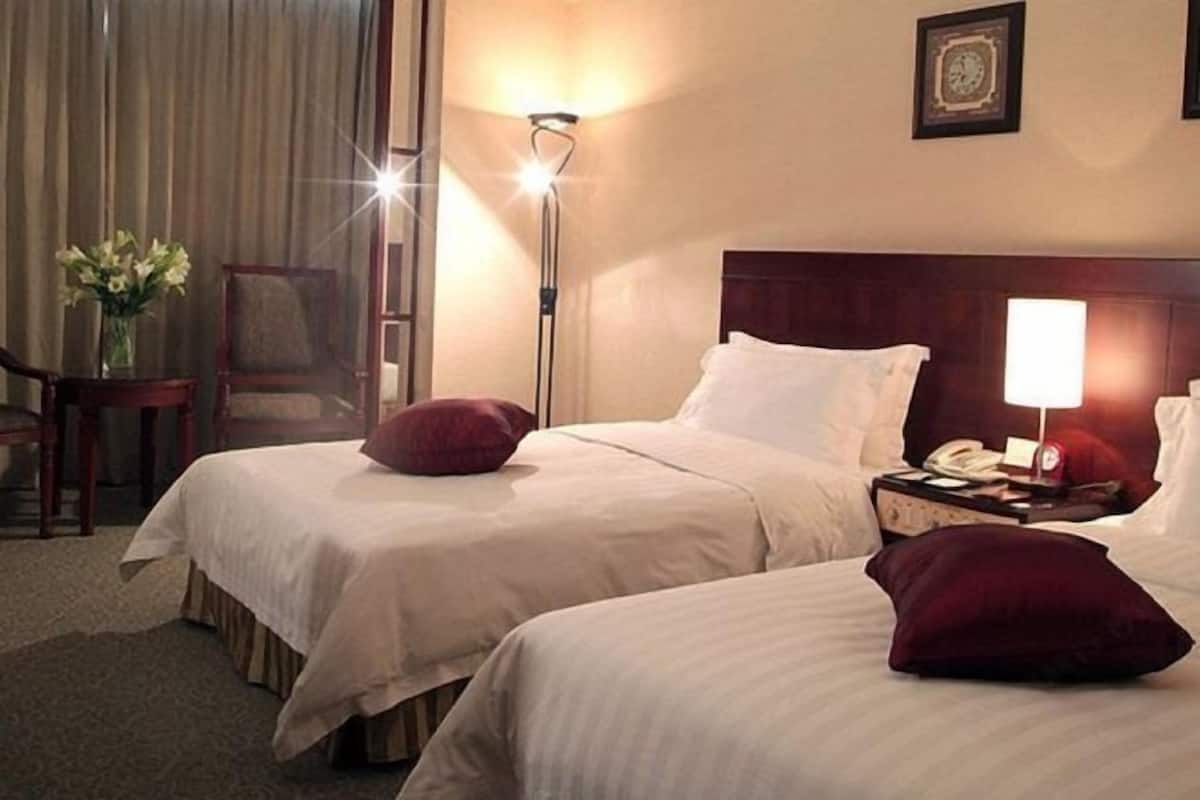A hotel room with two beds, a nightstand with a lamp, a chair, and a vase with flowers.