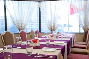 Un espace repas avec des tables dressées, offrant une vue sur la ville grâce à de grandes fenêtres.