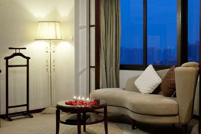 Sala de estar com sofá, luminária, mesa com velas e vista para o horizonte urbano pela janela.