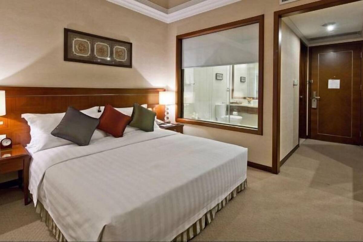 A hotel room with a large bed, a nightstand, a bedside table, a mirror, and a door.
