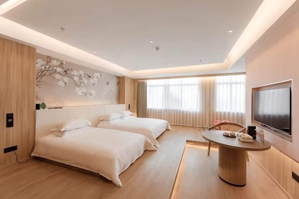 A hotel room with two beds, a TV, a desk, and a large window.