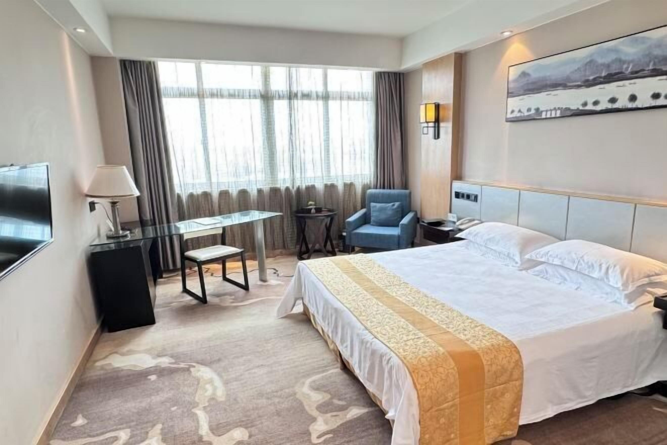 A hotel room with a bed, a desk, a chair, a TV, and a window with curtains.