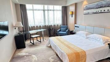 A hotel room with a bed, a desk, a chair, a TV, and a window with curtains.