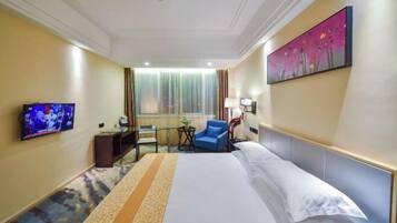 A hotel room with a bed, a TV, a desk, a chair, and a painting on the wall.