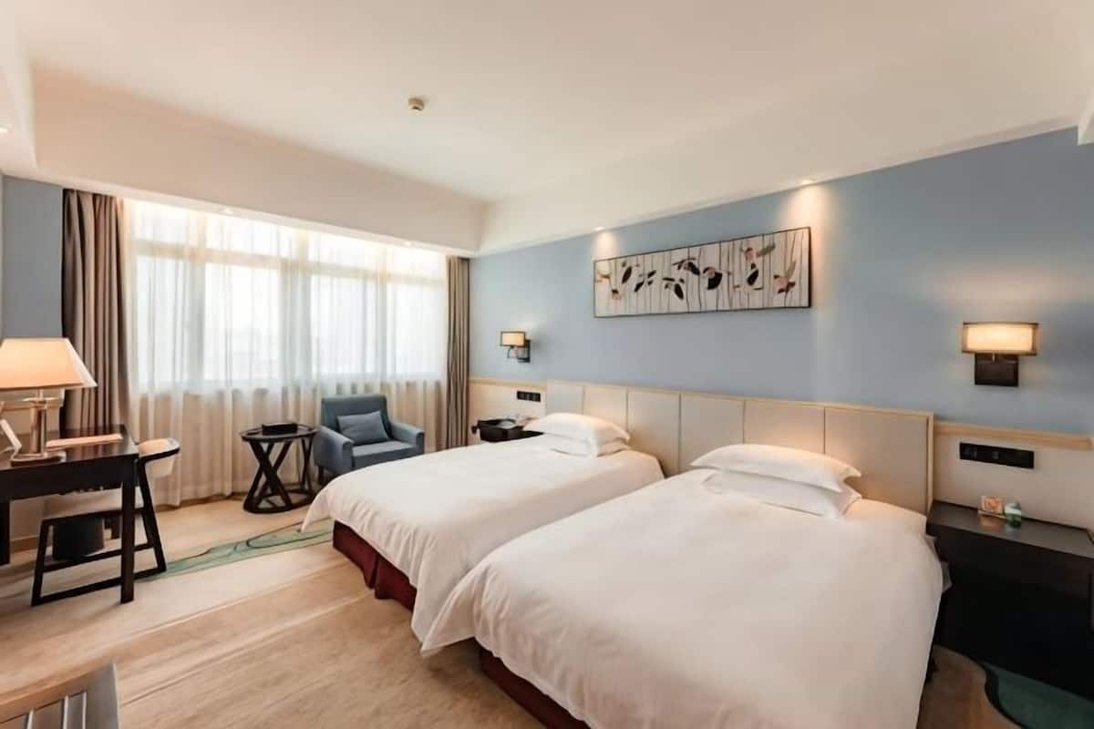 A hotel room with two beds, a desk, a chair, a nightstand, and a wall-mounted artwork.