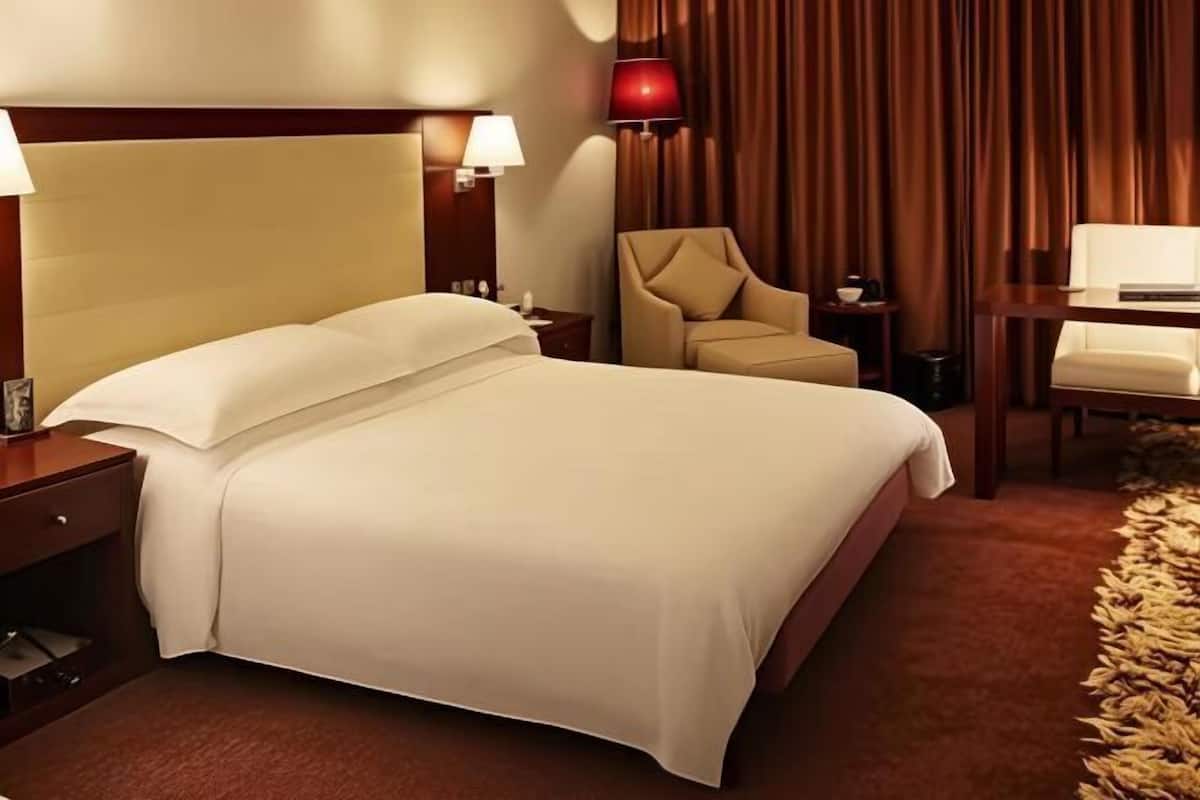 A hotel room with a large bed, a chair, a desk, and a lamp.