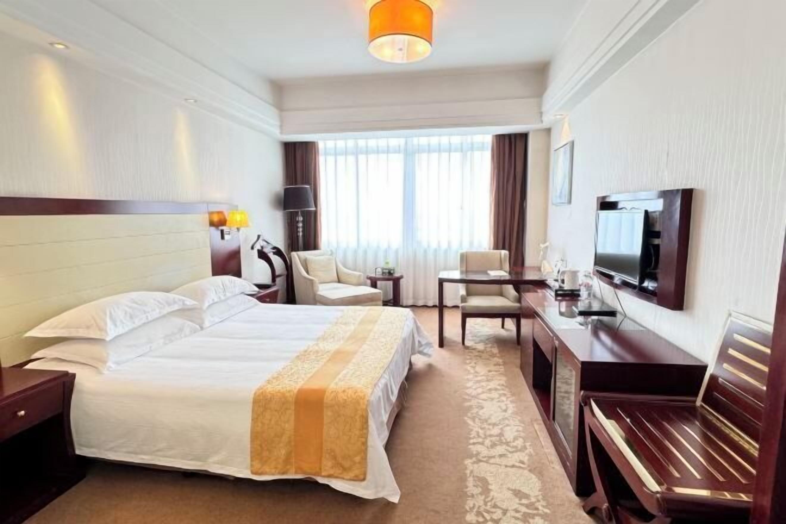 Habitación de hotel con una cama grande, un escritorio, una silla, un televisor y una ventana con cortinas.