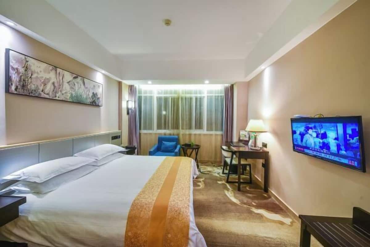 A hotel room with a bed, a desk, a chair, a television, and a window with curtains.