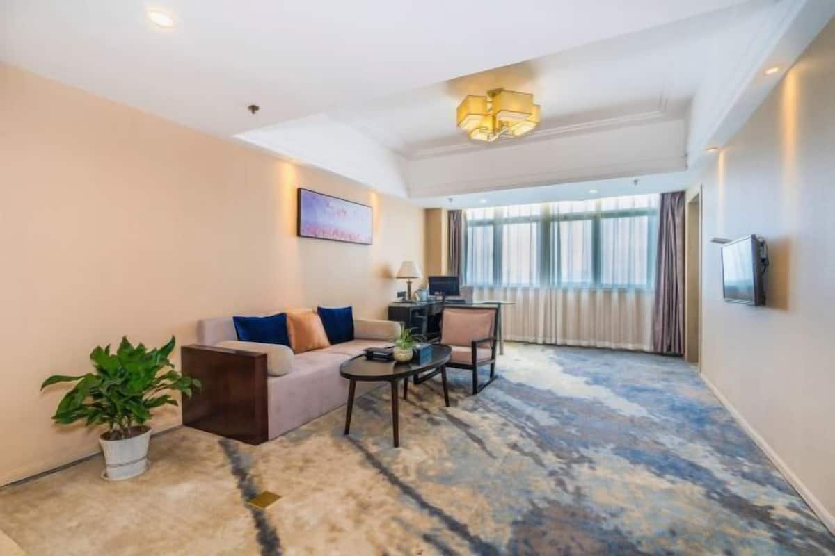 A modern hotel room with a sofa, armchair, coffee table, and a large window with curtains.