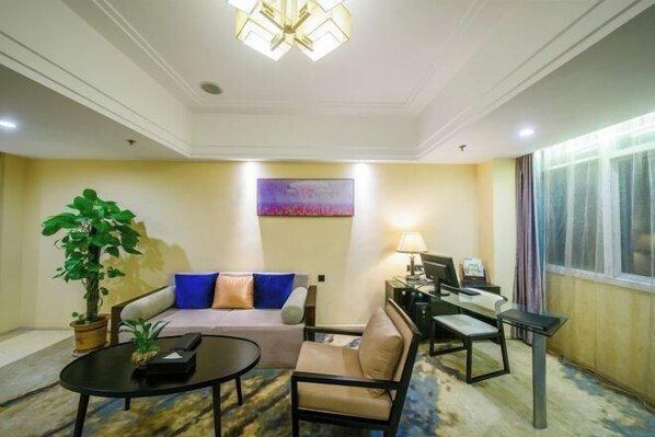 Habitación de hotel con sofá, escritorio, silla, mesa de centro, lámpara y ventana grande.