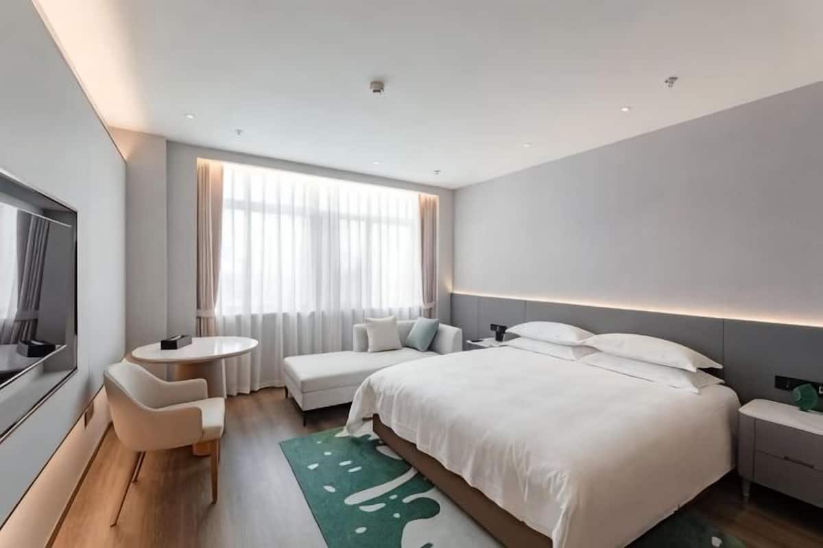 A modern hotel room with a large bed, a desk, a chair, a TV, and a window with curtains.