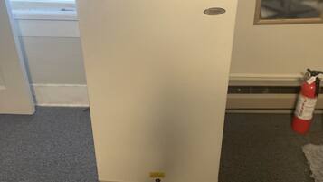 Un refrigerador blanco en una habitación con una ventana, un extintor y un cuadro en la pared.