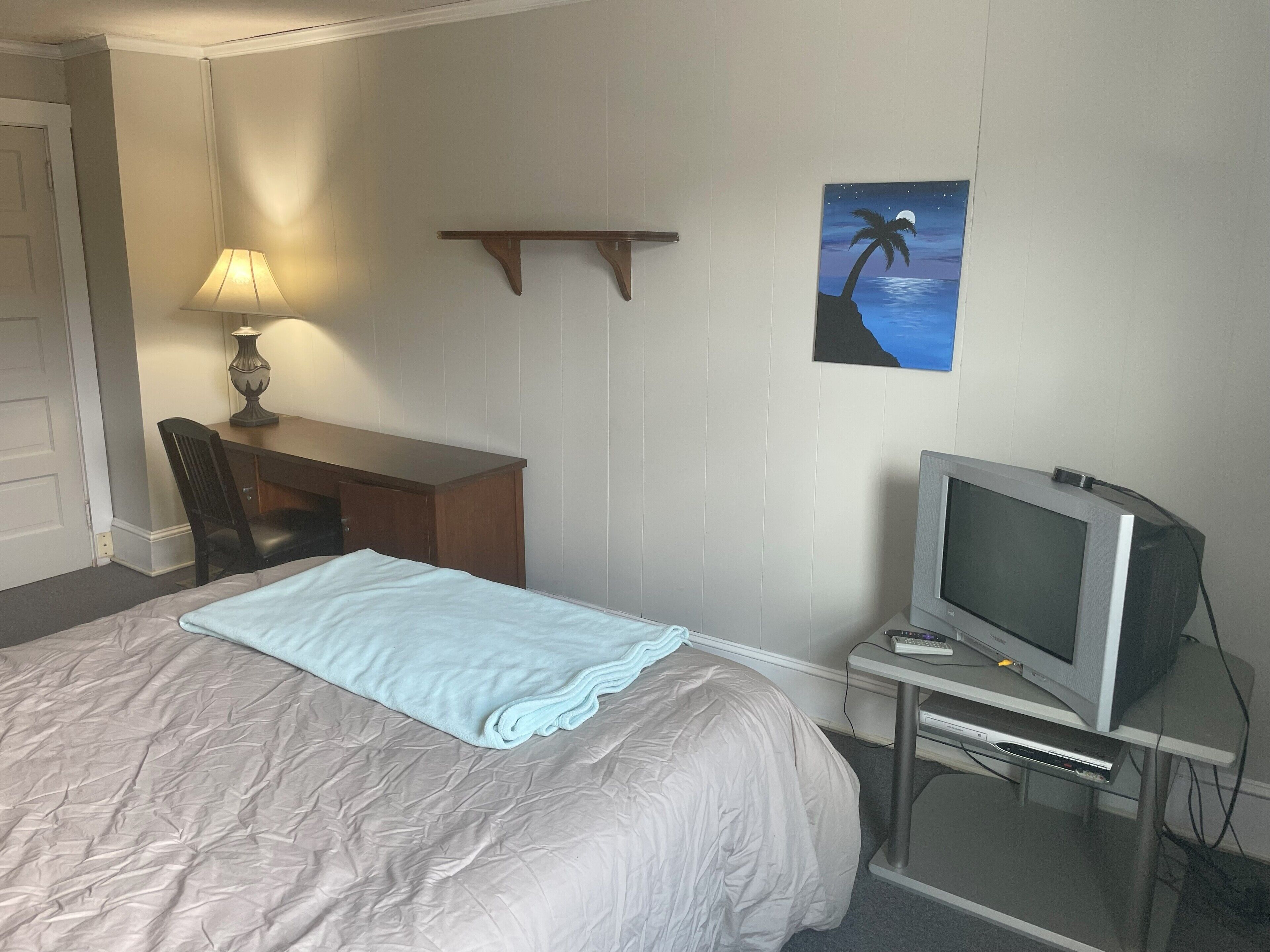 Une chambre d’hôtel équipée d’un lit, d’un bureau, d’une chaise, d’une télévision et d’une étagère fixée au mur.