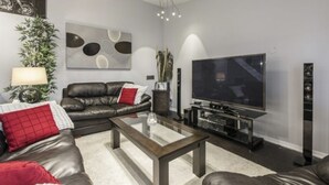 A modern living room with a leather sofa, a coffee table, a flat-screen TV, and a decorative wall piece. - Executive / Family Home | 2 BR • Office • Parking • 10mins to Toronto or Pearson (Mississauga)