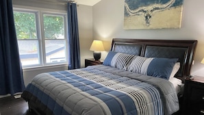 A bedroom with a bed, a nightstand, a lamp, a window with curtains, and a wall-mounted artwork. - Executive / Family Home | 2 BR • Office • Parking • 10mins to Toronto or Pearson (Mississauga)