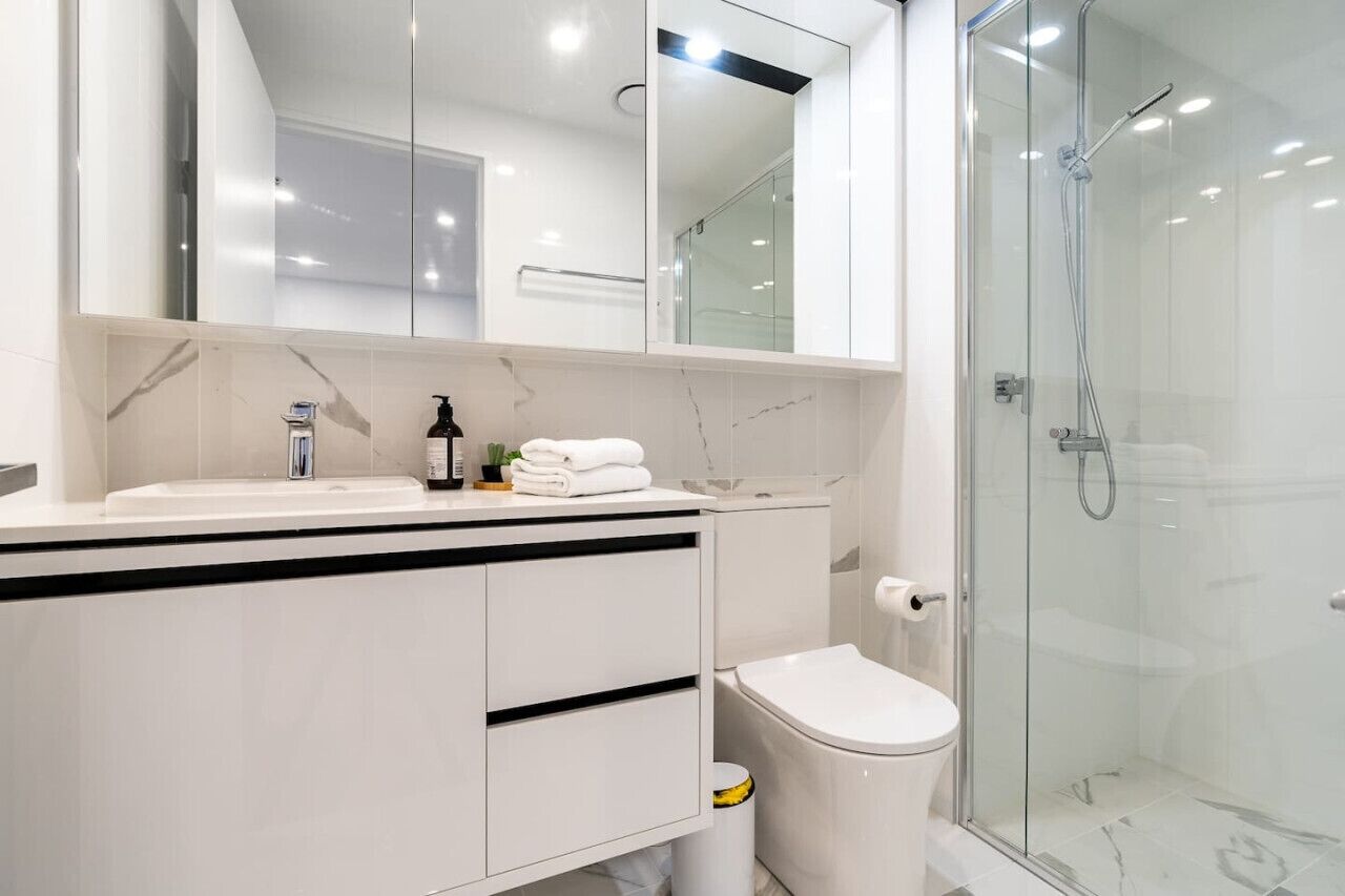 A modern bathroom with a glass shower enclosure, a white sink with a marble countertop, and a toilet.