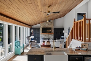A spacious living area with a stone fireplace, a large TV mounted on the wall, and a wooden ceiling.