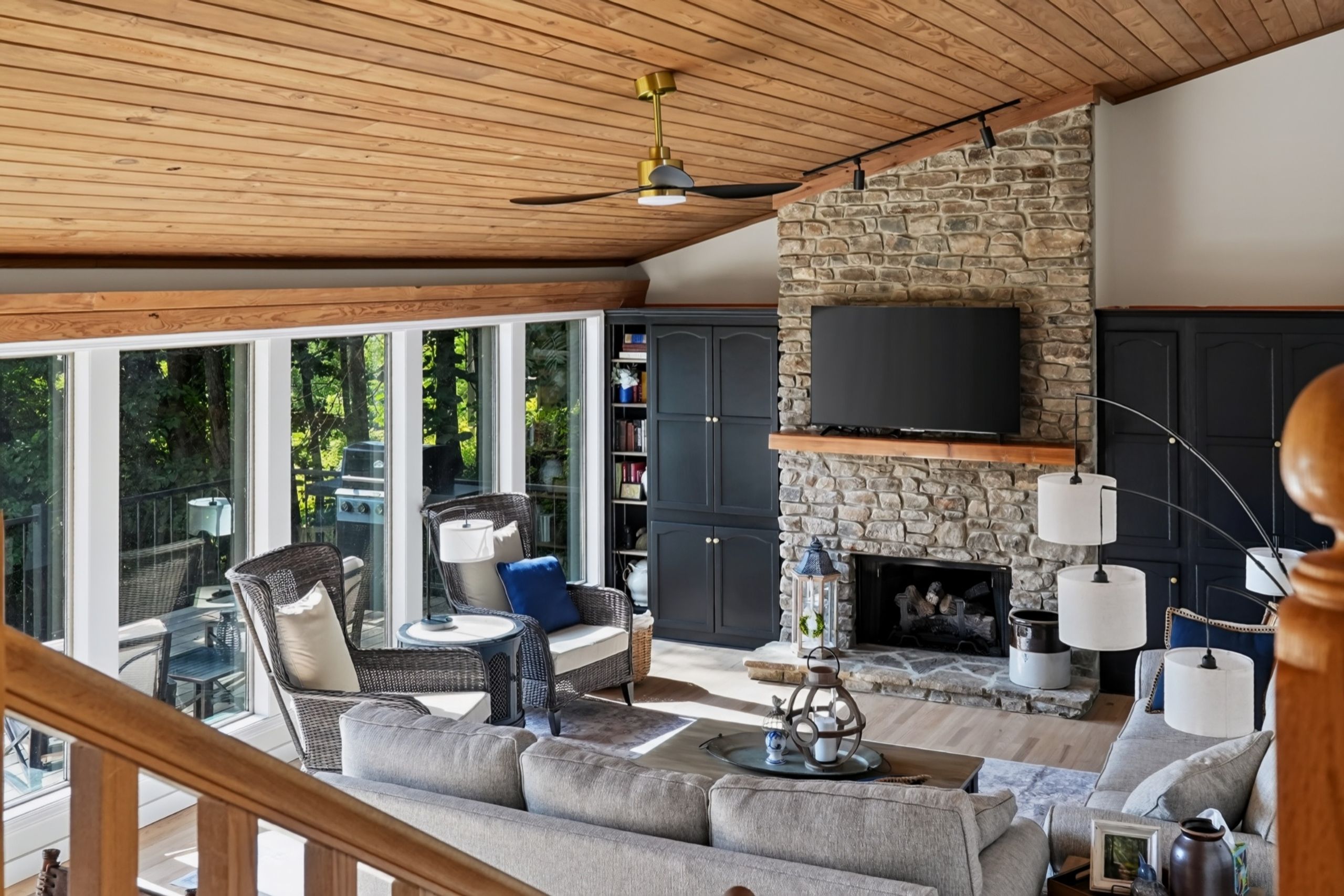 A spacious living area with a stone fireplace, a television mounted on the wall, and a large window overlooking greenery.