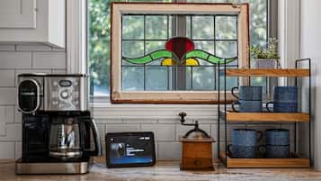 Una cucina con una macchina da caffè, una sveglia digitale, un macinino per caffè in legno e una finestra con un motivo a vetri colorati.