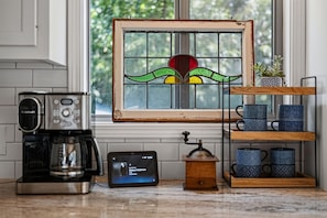 A kitchen with a coffee maker, a digital clock, a wooden coffee grinder, and a window with a stained glass design.