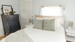 Een keurig opgemaakt slaapkamer met een bed, een dressoir, een nachtkastje en een raam met gordijnen.