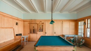 Een pooltafel in een ruimte met houten lambrisering, een tafeltje en een stoel.