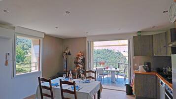 Un coin repas avec une table dressée pour quatre personnes, une cuisine équipée d’appareils modernes et un balcon offrant une vue panoramique.