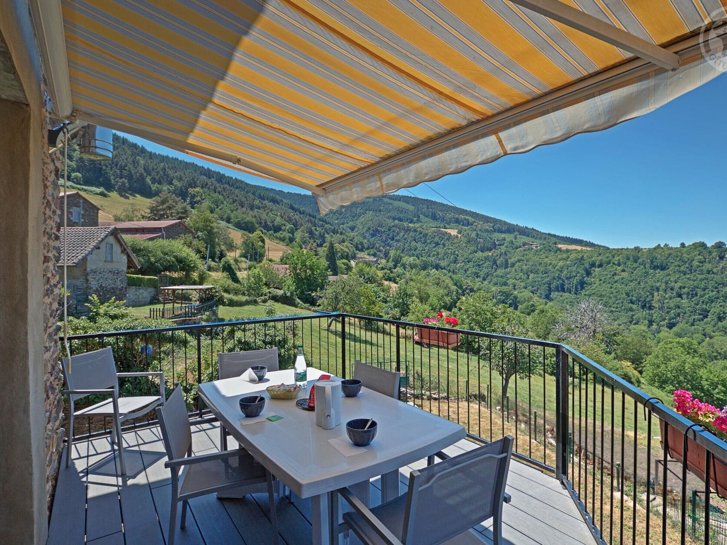 Una terraza con mesa y sillas, un toldo amarillo y vistas de un paisaje montañoso.