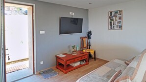 A living room with a television, a small table with a plant, a framed photo collage, and a door leading outside.