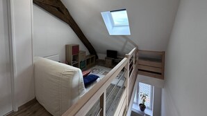 Slaapkamer in een loft met schuine wanden, dakraam, een bed, bureau en een klein raam met een plant.