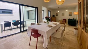 A dining area with a long table, chairs, and hanging wicker lamps. - Cozy New Cottage Near Beach with Private Terrace, Hot Tub, and EV Charger (Pornic)