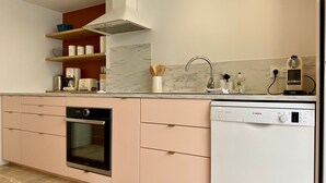 A modern kitchen with a built-in oven, dishwasher, and a coffee machine. - Cozy New Cottage Near Beach with Private Terrace, Hot Tub, and EV Charger (Pornic)