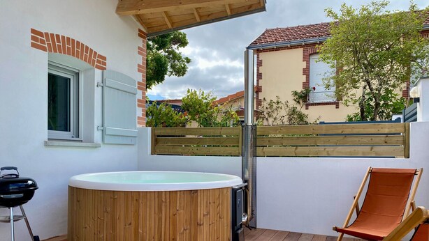 A wooden deck with a hot tub, a grill, and a folding chair. - Cozy New Cottage Near Beach with Private Terrace, Hot Tub, and EV Charger (Pornic)