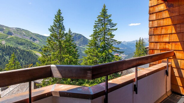 Ein Balkon mit Holzgeländer, der auf eine gebirgige Landschaft mit immergrünen Bäumen blickt.