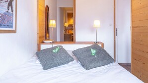 Ein Hotelzimmer mit einem Bett, zwei Kissen, einem Spiegel, einem Bild und einer Holztür.