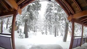 Ein verschneiter Außenbereich mit einer Holzhütte, möglicherweise ein Kiosk, mit Blick auf einen verschneiten Wald.