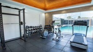 A gym with a treadmill, dumbbells, and a rowing machine, overlooking a swimming pool. - Holiday Suites Puerto Princesa (Puerto Princesa)