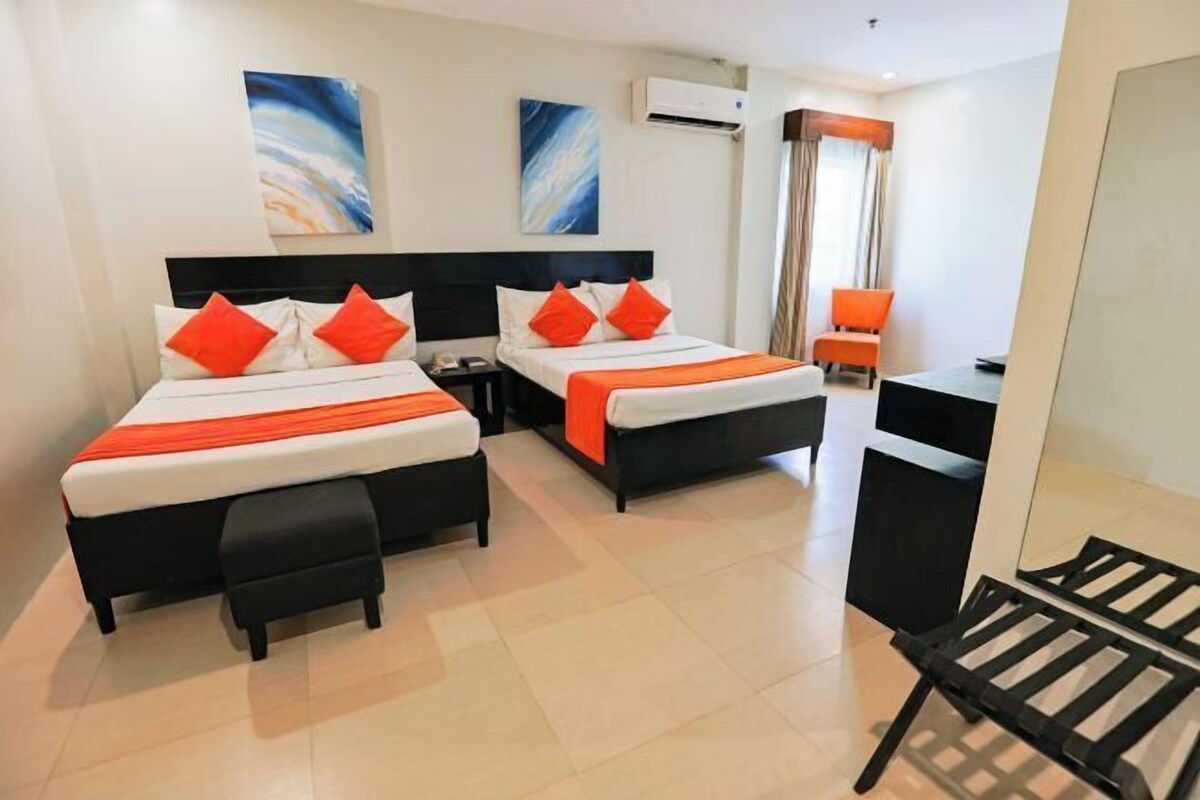 A hotel room with two beds, a desk, a chair, and artwork on the walls.