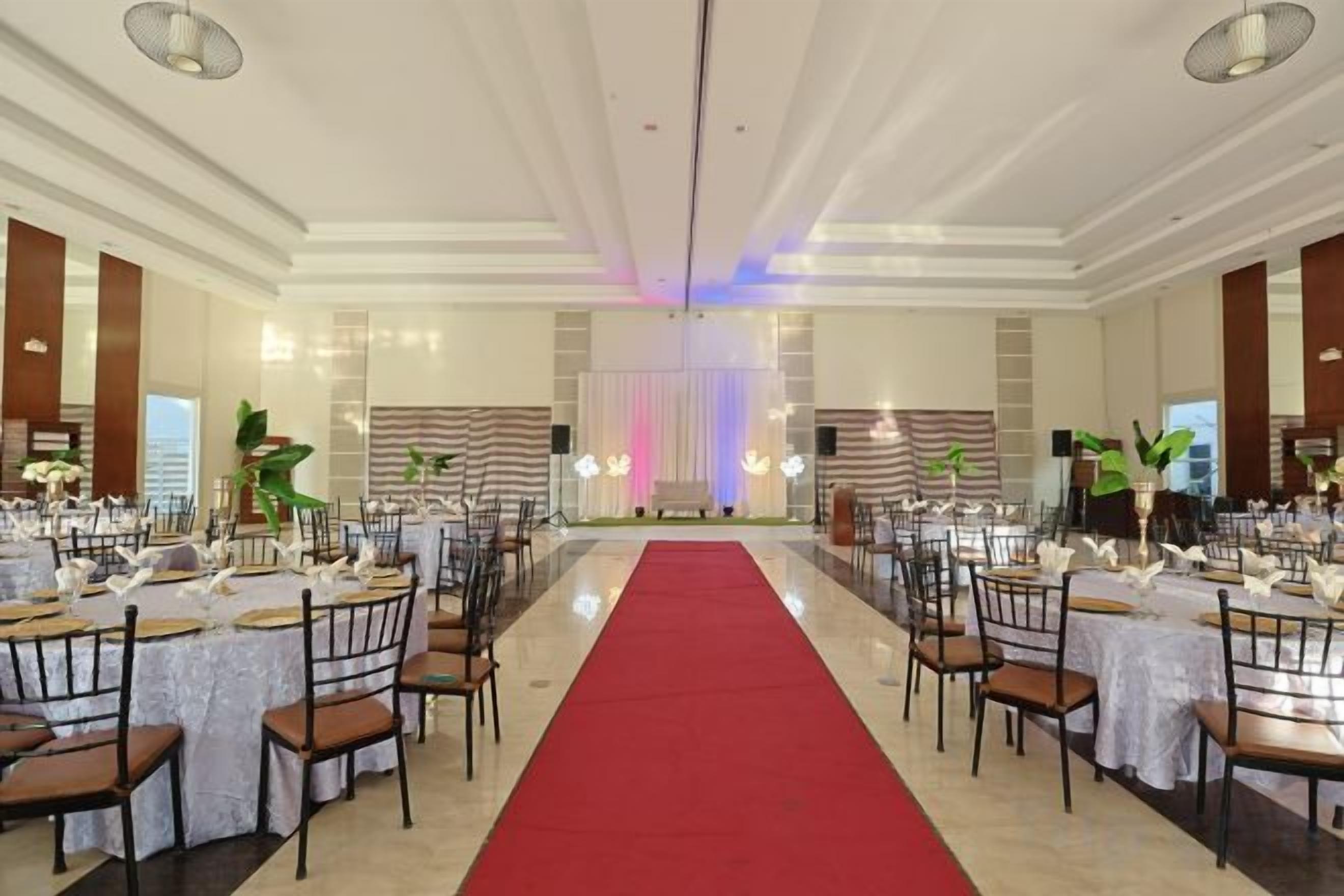 A banquet hall with round tables, chairs, a red carpet, and a stage with curtains.