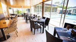 A restaurant with outdoor seating, wooden flooring, and large windows overlooking a pool. - Holiday Suites Puerto Princesa (Puerto Princesa)