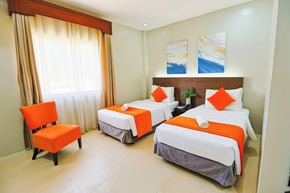 A hotel room with two beds, a chair, and two paintings on the wall.