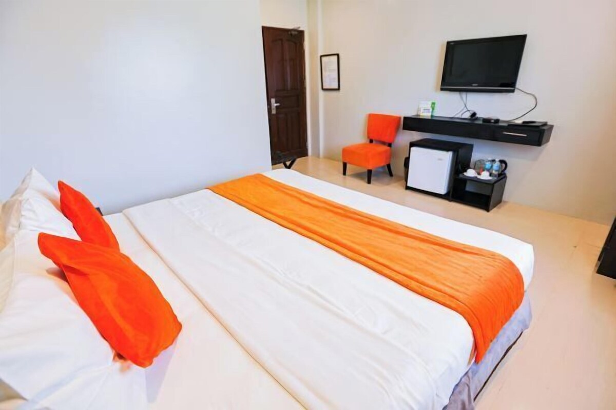 A hotel room with a bed, a desk with a computer, a television, and a small refrigerator.
