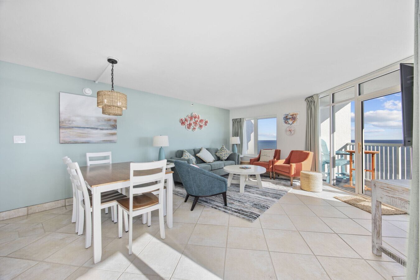 A spacious living area with a dining table, chairs, a sofa, and a coffee table. There is a balcony with a view of the sea.