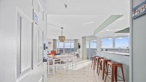 A spacious dining area with a view of the sea, a kitchen with a stone backsplash, and a bar area with stools. - Penthouse SeaWatch Ocean Front (Myrtle Beach)